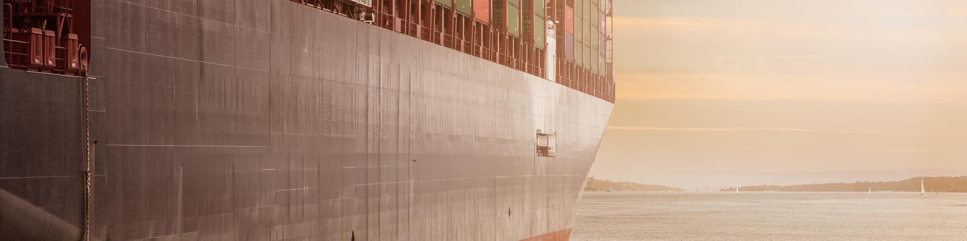 A cargo ship with the sea and sailboats in the background