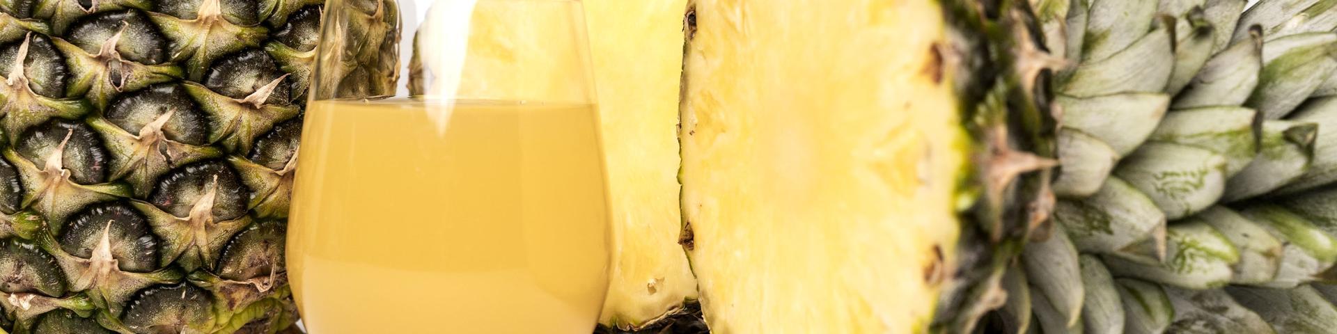 A cut open fresh pineapple alongside a glass of pineapple juice