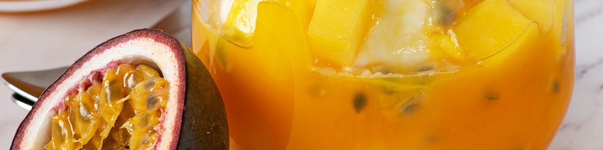  A halved passionfruit next to a glass of passionfruit and mango drink