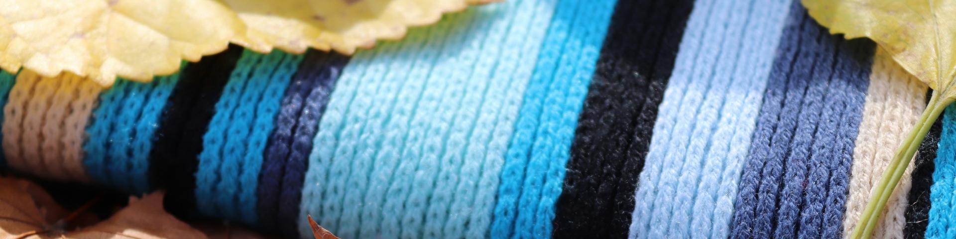 A knitted scarf in blue tones with leaves lying on top of it