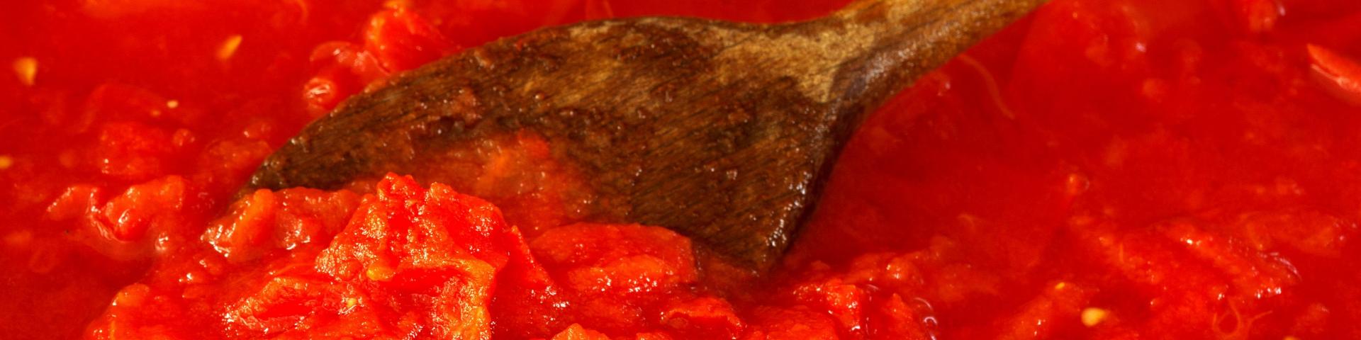 A large wooden spoon stirring tomato puree
