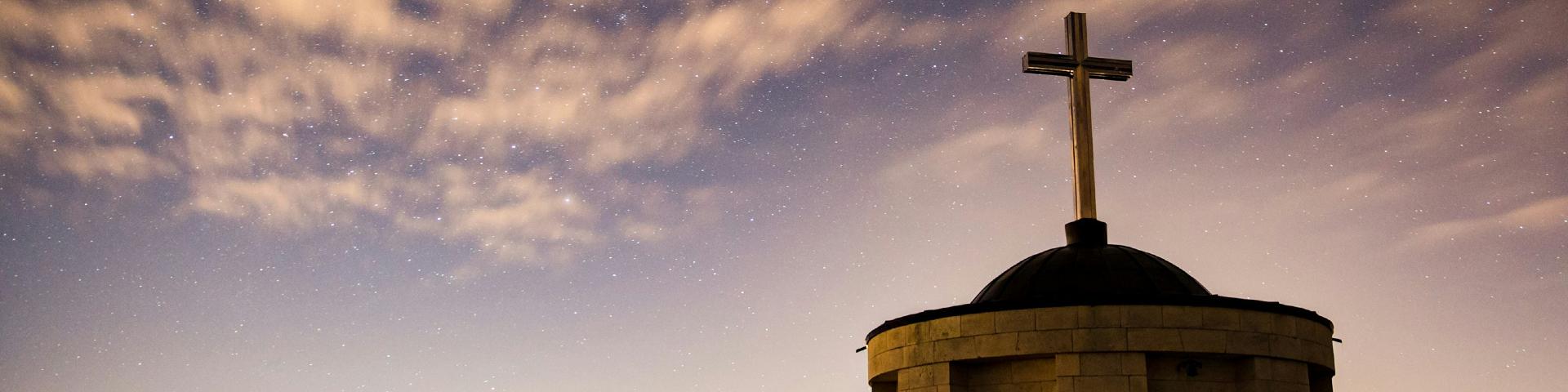 A small brick church with a cross on it, with the night sky in the background
