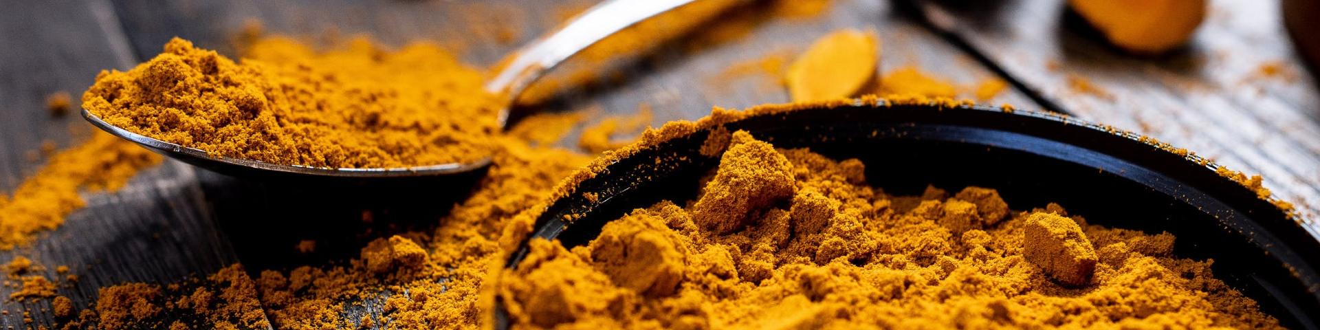 A small metal spoon filled with turmeric powder, alongside a bowl of turmeric powder