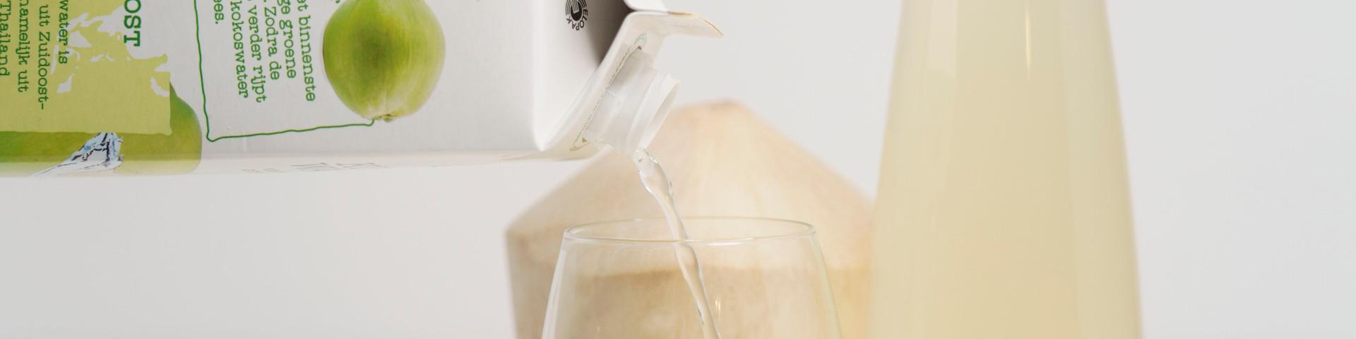 Coconut water being poured into a glass, with coconut water and coconut meat in the background