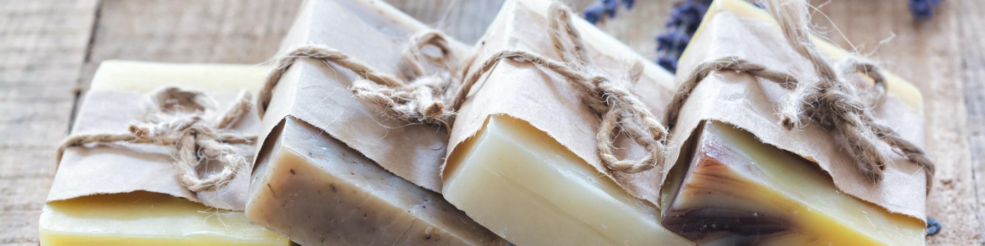 Four soap bars wrapped in packaging, lying on a wooden table
