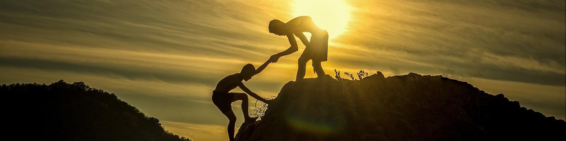Shadows of two boys climbing a hill with the sun in the background