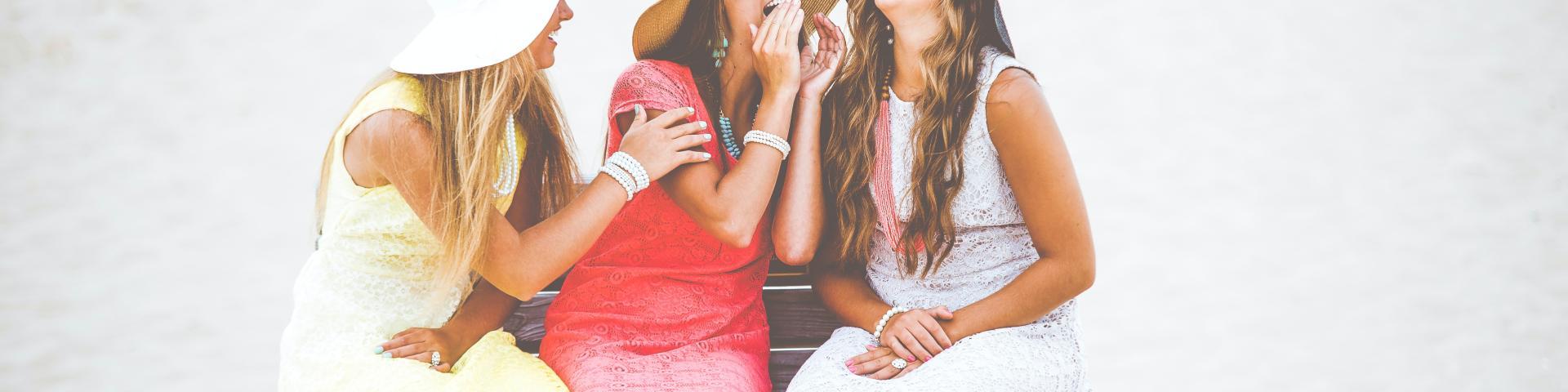 Three women wearing dresses talking with one another