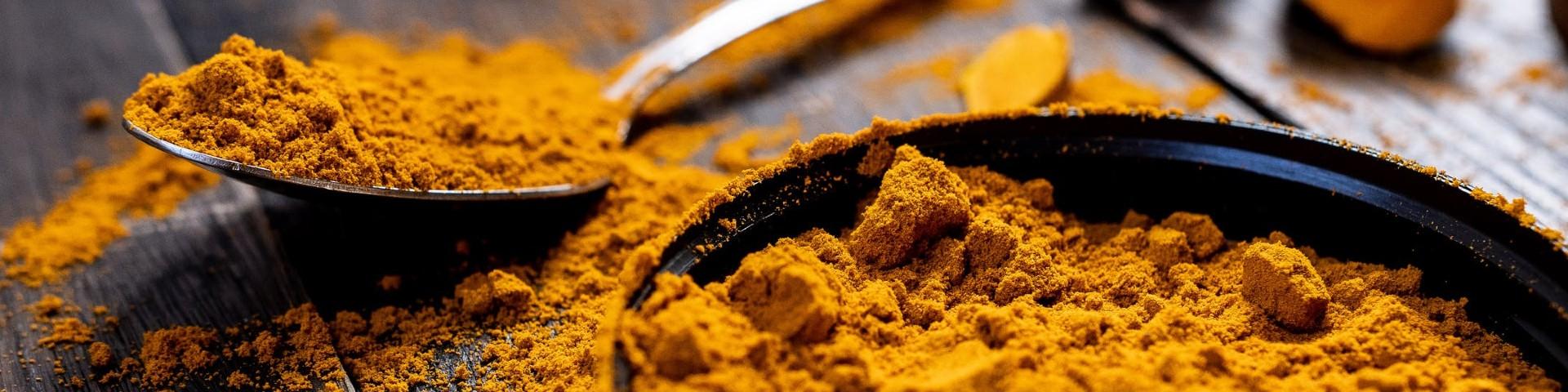 Turmeric powder in a shallow dish and on a metal spoon, with some powder spilling out on the table below.jpg