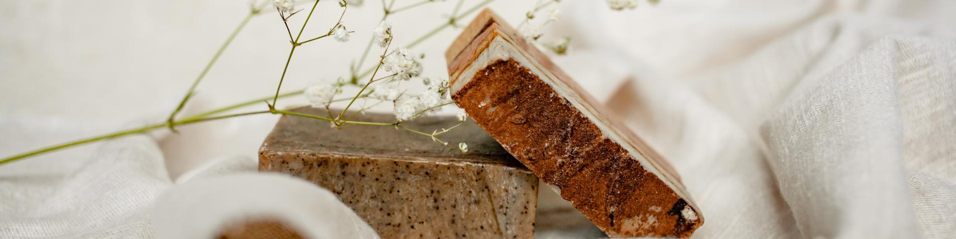 Two bars of soap with a plant placed on them, lying on a piece of white textile