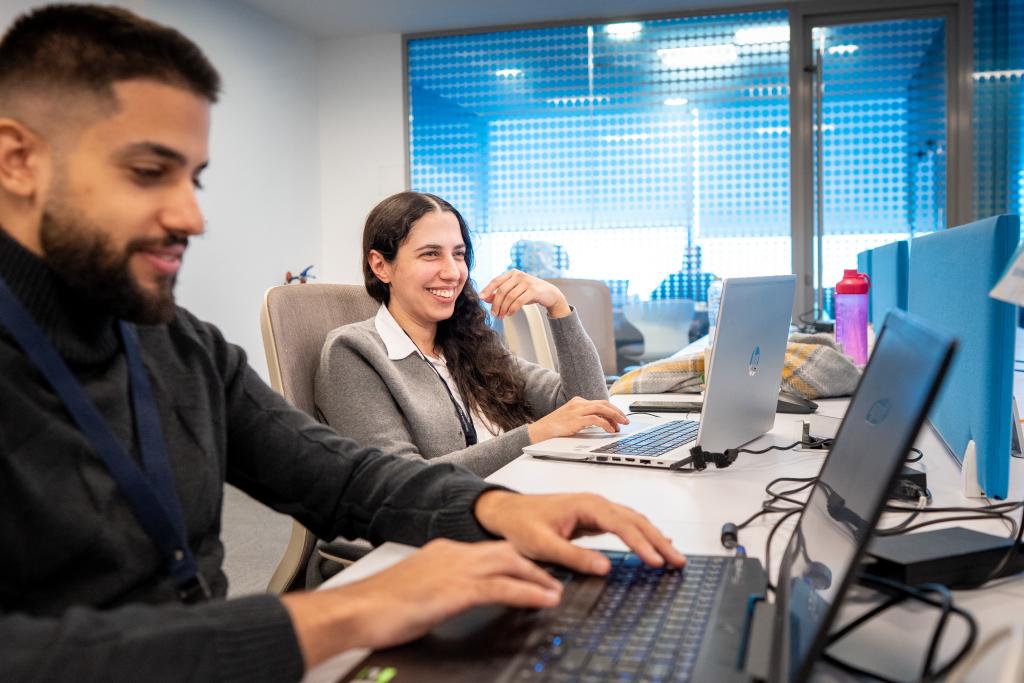 Young man and woman behind their laptops, smiling