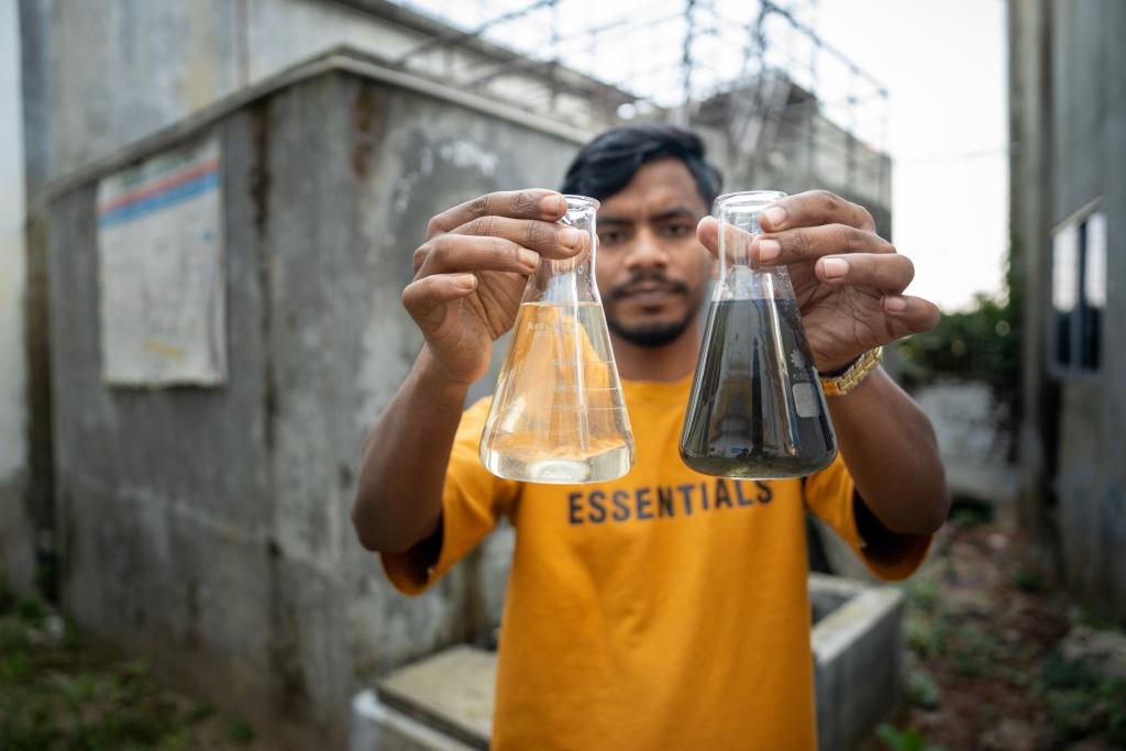 Man holding two glass bottles in front of him, one with clear water, one with dirty water