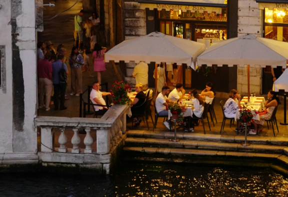 People sitting at a terrace near a canal at night