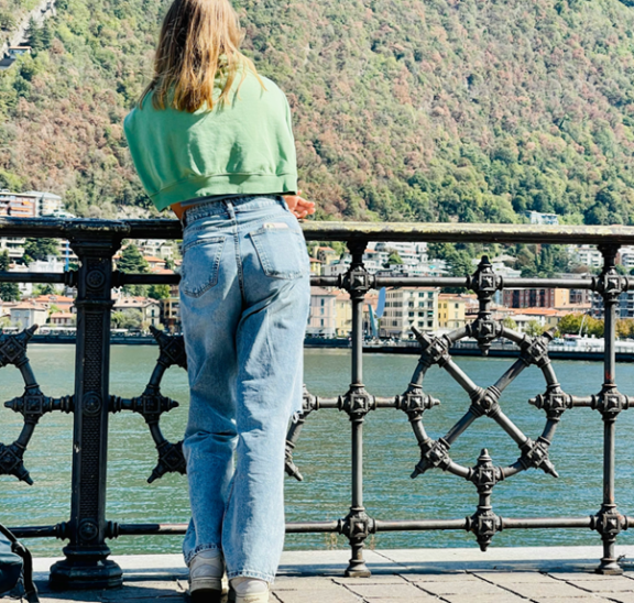Person leaning on a fence, seen from behind, with green top and light blue jeans