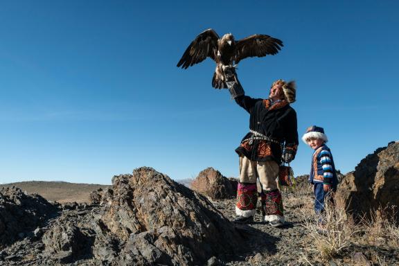 Man and boy in traditional clothes. The man is letting an eagle land on his hand.