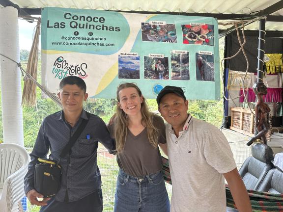 Three people posing for a photo together in front of a marketing stand for agritourism
