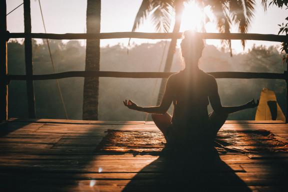 Person practising yoga on a wooden veranda while the sun is setting