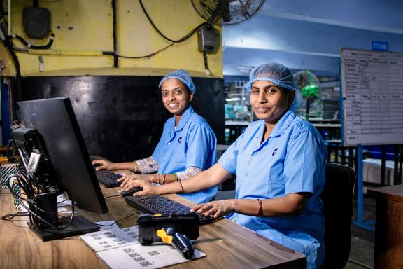 Two persons wearing blue lab shirts and hair nets working at a desk