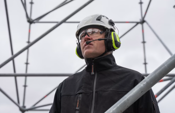 Person with workwear consisting of a black vest, a helmet and safety glasses