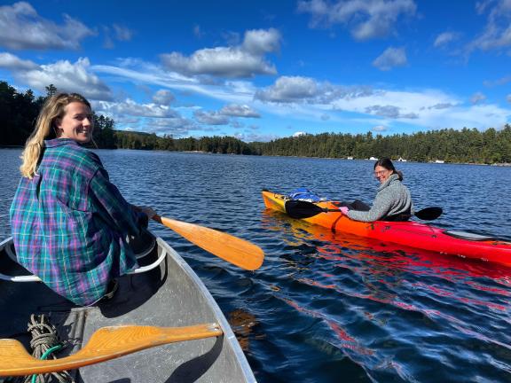 Two women paddling in canoes, looking back and smiling