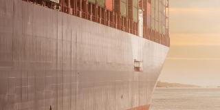 A cargo ship with the sea and sailboats in the background