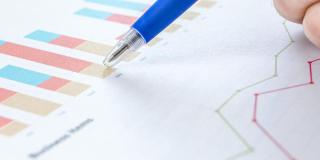 A hand pointing a pen at a bar chart, with a line graph under it