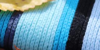 A knitted scarf in blue tones with leaves lying on top of it