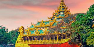 A red and golden boat with a religious site and trees in the background