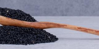 A wooden spoon filled with black cumin seeds, resting on a pile of black cumin seeds.jpg