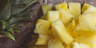Pieces of pineapple sitting in a bowl on a table, with the crown of a pineapple beside it